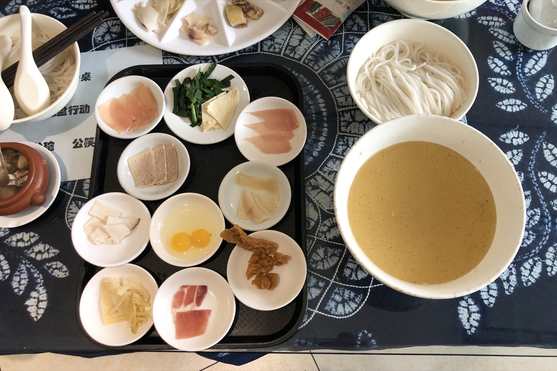 Crossing-the-bridge rice noodles with broth, rice noodles, and small ingredient plates in Yunnan.