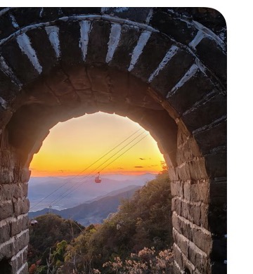 Sunset view through a Mutianyu Great Wall arch with mountains and cable cars.