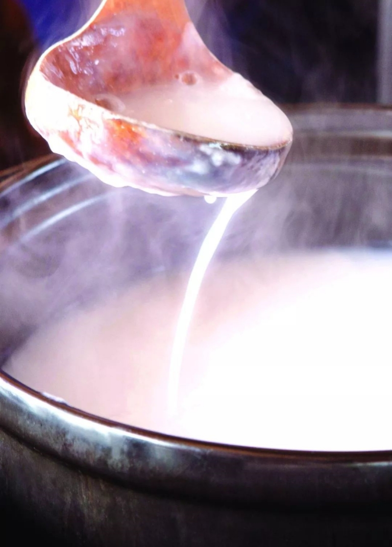 A spoon lifting silky porridge hot pot broth from a steaming pot.